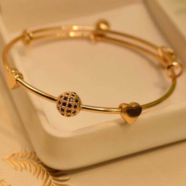 Gold bangle bracelet with heart-shaped charms and a detailed bead.